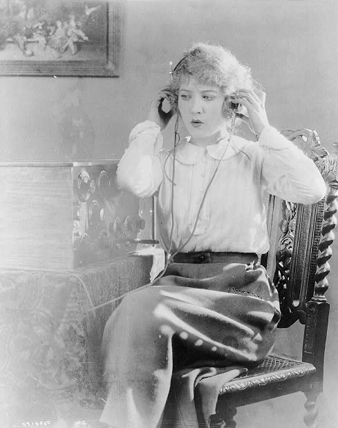 A young woman in a 1920 blouse adjusting radio headphones over her ears